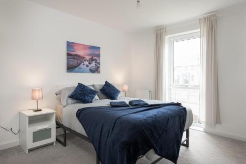 Schlafzimmer mit einem Bett mit blauer Bettwäsche und einem Fenster in der Unterkunft Two Bedroom Apartment - Milton Keynes By Aryas Properties in Broughton