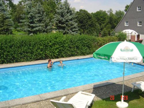 two people in a swimming pool with an umbrella at Gaststätte & Pension Alte Mühle in Dorfchemnitz