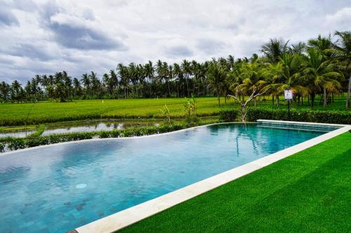 uma piscina com relva verde e palmeiras em Adil Villa & Resort em Ubud