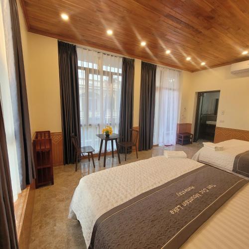 a bedroom with two beds and a table and windows at Tam Coc Mountain Lake Homestay in Ninh Binh