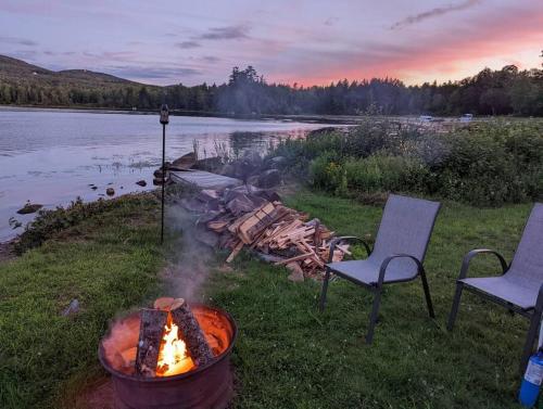 a fire pit in the grass next to a lake at Lakefront Stunning Home, only 30 min to Sugarloaf! in New Portland