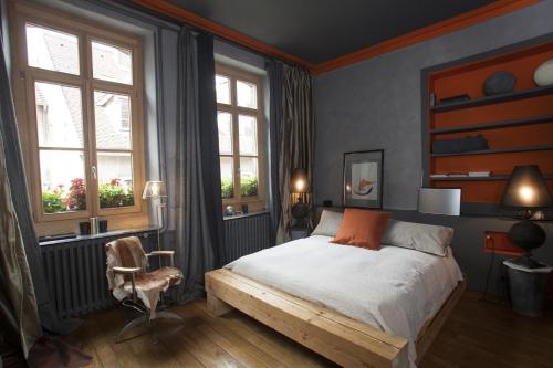 a bedroom with a bed and a chair and windows at La Maison d'A Côté in Pontarlier