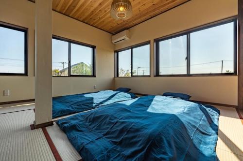 a bedroom with a large blue bed in a room with windows at 思い出になる九十九里の古民家ドマノマ ハンモック バーベキュー in Kujukuri