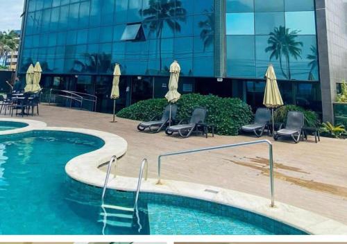 una piscina frente a un edificio con sillas y sombrillas en Flat Suites Super Luxo, en Maceió
