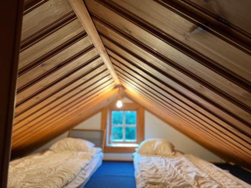 two beds in a room with wooden ceilings and a window at Highnoon Westernranch guesthouse in Ljusdal