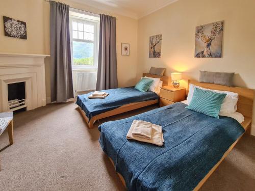 two beds in a room with a fireplace at Lochside House in Stronachlachar