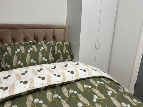 a bed with a green and white comforter and a bedskirts at Park View Serviced Apartment - Next to Northolt Tube Station - Near Central London & Wembley in Northolt