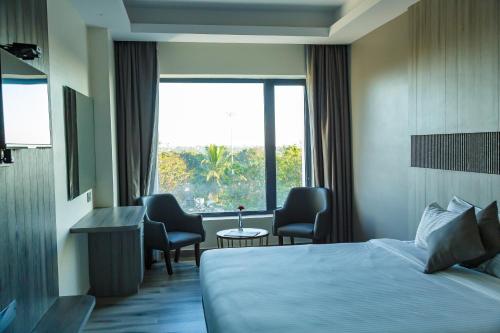 a hotel room with a bed and chairs and a window at Hotel Galore Inn in Mysore