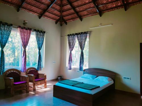 a bedroom with a bed and two chairs and windows at Memories of Malnad in Chikmagalūr