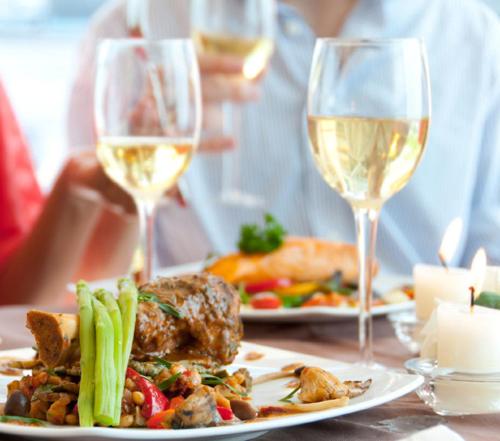 a table with two plates of food and glasses of wine at 't STRANDHUYS en DE VUURTOREN, met eigen KEUKEN, ZONNIG TERRAS nabij DORP, DUINEN en STRAND, Incl verwarmd binnen ZWEMBAD in Hollum