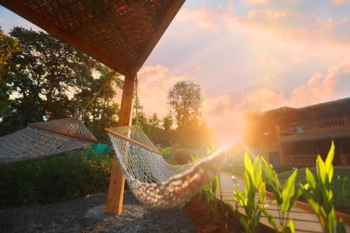 a person holding a hammock in a backyard with the sun setting at One At Goa in Canacona