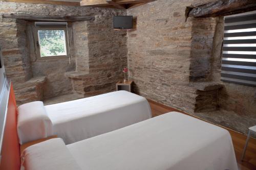 two white beds in a room with a stone wall at Albergue Turistico Salceda in Salceda