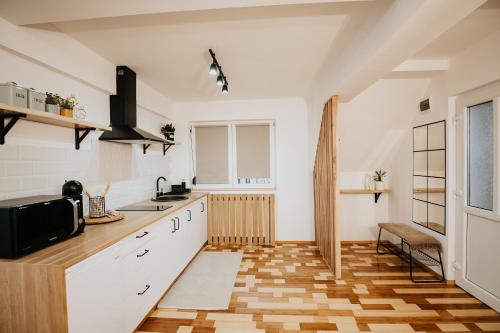 a kitchen with white cabinets and a wooden floor at DOUX Apartman in Odorheiu Secuiesc