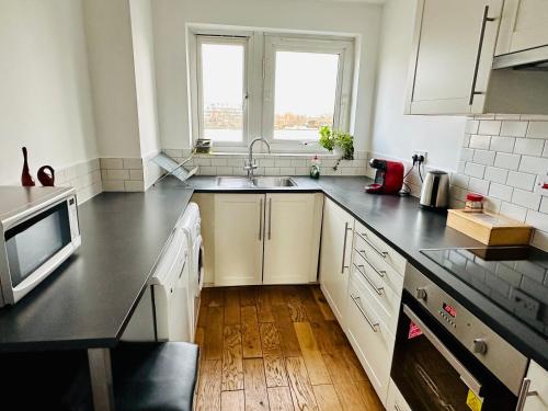 a kitchen with white cabinets and a black counter top at X Leysdown Apartment Camden in London