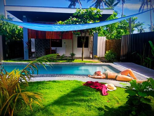 una mujer tumbada en el césped junto a una piscina en Amara Family 2Br House, pool, 180Mbps, garden , parking Central location, en General Luna
