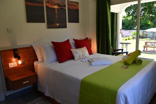 1 dormitorio con 1 cama grande con almohadas rojas y verdes en ANV HOLIDAY APARTMENTS en Grand'Anse Praslin
