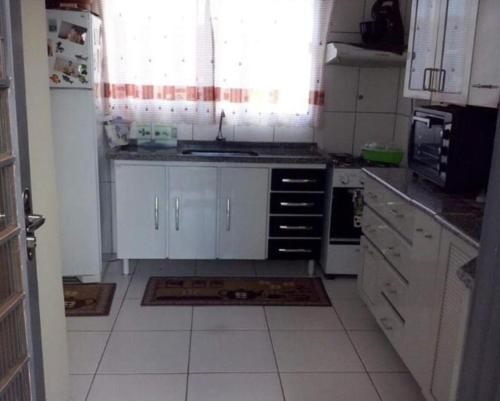 a kitchen with white cabinets and a white tile floor at Casa aconchegante in Campo Grande