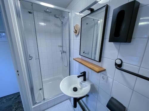 ein Bad mit einem Waschbecken, einer Dusche und einem Spiegel in der Unterkunft Hotel de Slapende Hollander in Kaatsheuvel