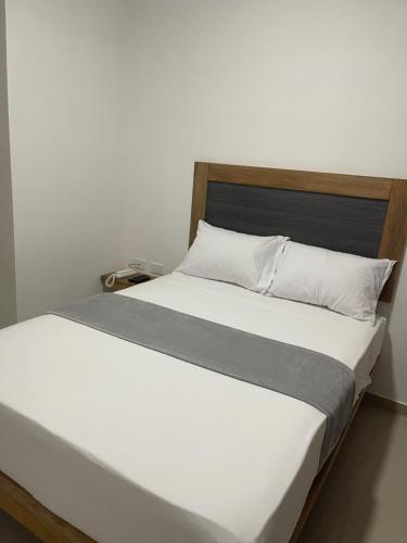 Cama blanca con cabecero de madera y almohadas blancas en Hotel El Faro, en Cartagena de Indias
