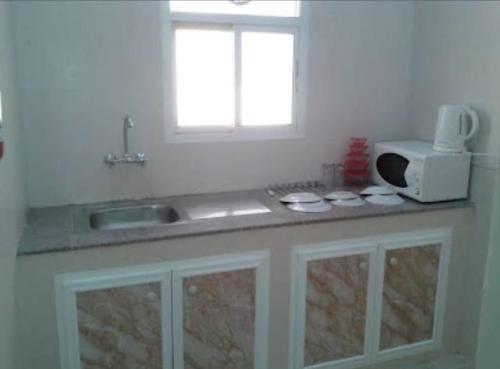 a kitchen counter with a sink and a microwave at Al Basateen Hotel Apartment in Sur