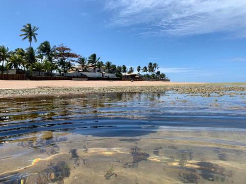 a beach with palm trees and a house in the distance at Bangalô Tavarua Itacimirim Pé na areia in Itacimirim