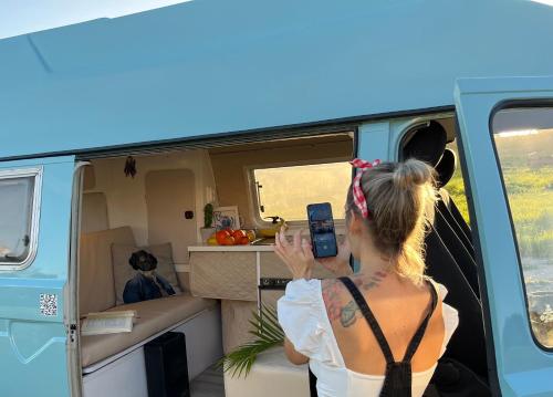 a woman taking a picture of a camper with her cell phone at Rent a BlueClassics 's campervan vw T3 azulina in Algarve au Portugal, in Portimão