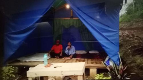 two men sitting inside of a blue tent at Glamping Kalimarno Wonosalam in Tukum