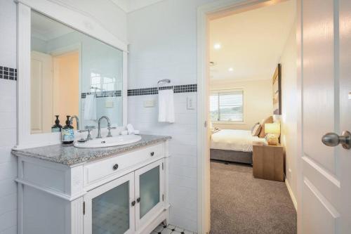 ein weißes Badezimmer mit einem Waschbecken und ein Schlafzimmer in der Unterkunft 'Vineyard Cottage' A Golden Escape among the Vines in Eurunderee