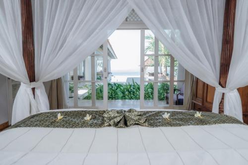 a bedroom with a bed with white curtains and a window at Raaga Samudra Villa in Padangbai