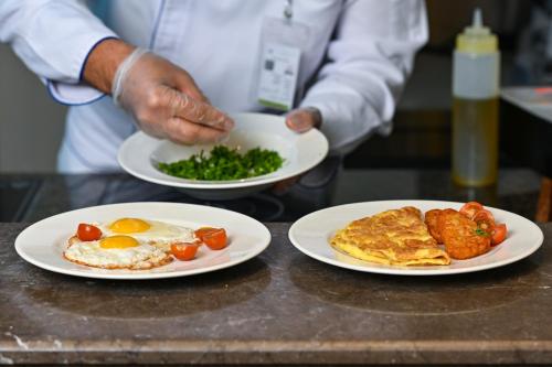 a chef holding two plates of food on a counter at Clarion Hotel Jeddah Airport in Jeddah