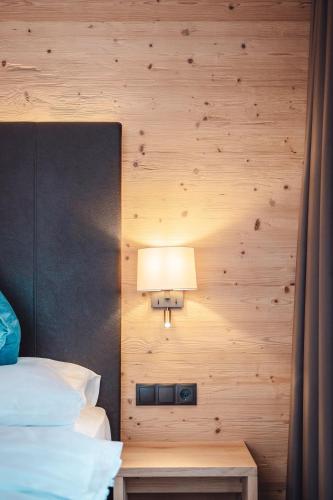 a bedroom with a wooden wall with a bed and a lamp at Hotel Plan de Gralba - das Berghotel in Selva di Val Gardena