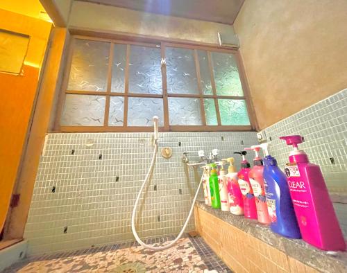La salle de bains est pourvue d'une douche et de nombreuses bouteilles sur la corniche. dans l'établissement 自然豊かな隠れ家 ゲストハウス和村Nagomura, à Shimonoseki