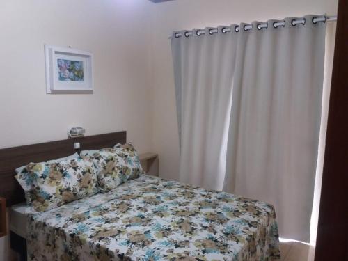 a bedroom with a bed with a floral bedspread and a curtain at Casa em Torres Praia da Cal in Torres