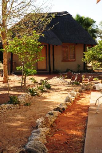 a house with a thatched roof and a dirt road at Beenbreck Guest Farm in Windhoek Noord