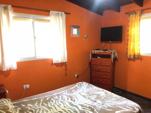 1 dormitorio con paredes de color naranja, 1 cama y TV en Cabaña Hakuna Matata en Santa Rosa de Calamuchita