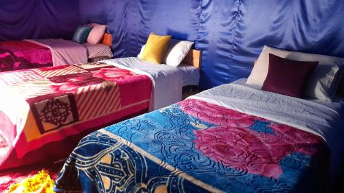 a room with two beds with colorful blankets and pillows at Oasis enchantée in Merzouga