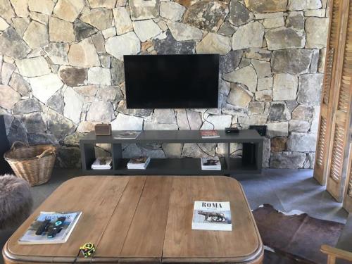 a living room with a table and a tv in a stone wall at Casa grande barrio Rumenco in Mar del Plata