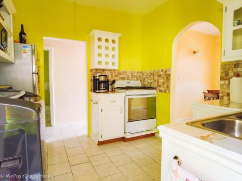 cocina con paredes amarillas y horno de fogón blanco en Coco Rose Apartments en Soufrière