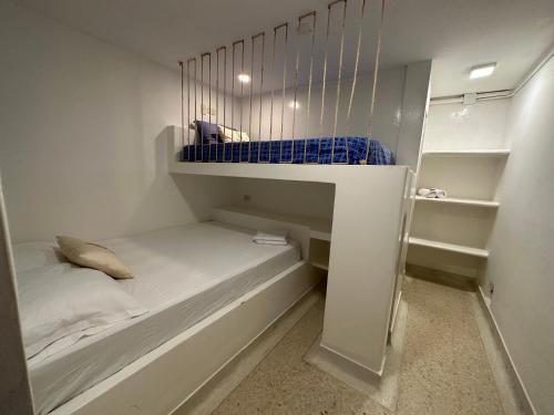 um pequeno quarto branco com uma cama e prateleiras em El Faro Hostel em Arboletes