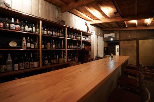 un homme debout derrière un bar avec des bouteilles d'alcool dans l'établissement 赭Soho Yunotsu Old Village Inn & Bar, à Ōmorichō