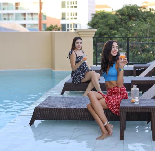 two women sitting on a bench next to a swimming pool at The Quba Boutique Hotel Pattaya in Pattaya Central