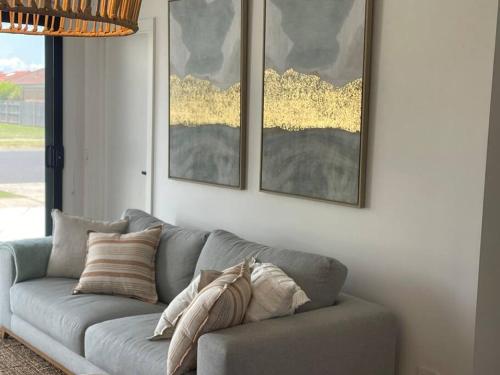 a gray couch in a living room with paintings on the wall at Quarterdeck Lakes Entrance 2br *Waterfront* Apartment in Lakes Entrance