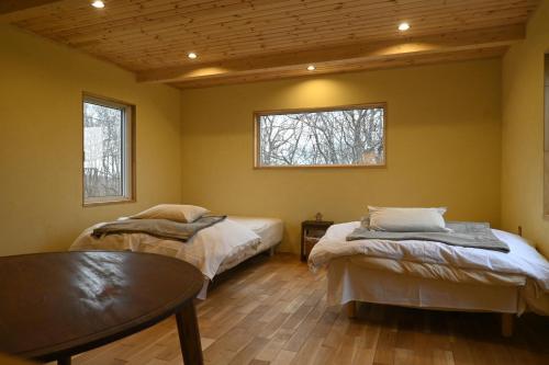 Habitación con 2 camas, mesa y 2 ventanas. en 小さな森の貸し切り宿Forest-House-Ranapirica, en Shibetsu