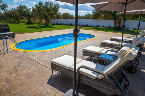 a swimming pool with lounge chairs and an umbrella at Old olive tree cottage in Áyioi Apóstoloi