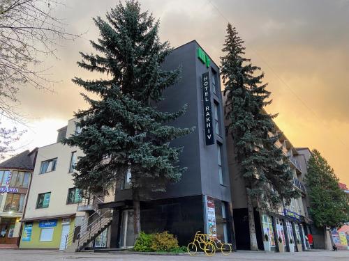 a building with two pine trees in front of it at Rakhiv Hotel & Apartments in Rakhiv