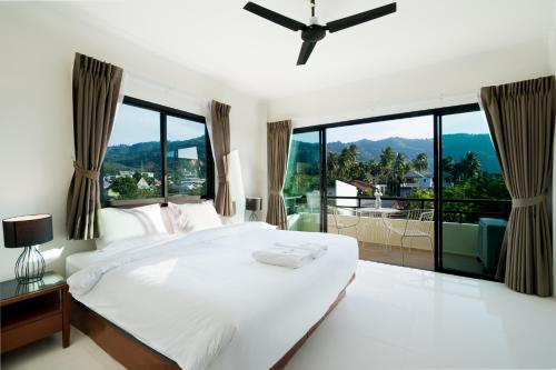 a bedroom with a large white bed and large windows at Hill Myna Holiday Park & Cafe in Bang Tao Beach