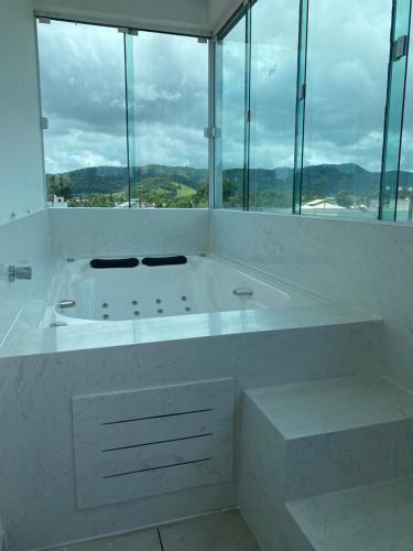 Baño blanco con bañera grande y ventanas en Apartamento Completo com Hidro, en Penha