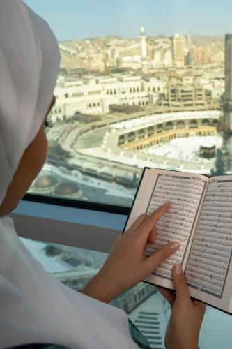 a woman reading a book in front of a window at Raffles Makkah Palace in Makkah