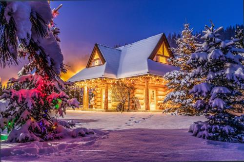 une cabane en rondins dans la neige avec des lumières de Noël dans l'établissement Chalet Wioska Jagny, à Poronin