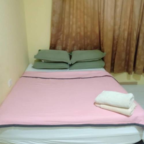 un letto con lenzuola rosa e cuscini verdi in una stanza di Home Stay JM a Shah Alam